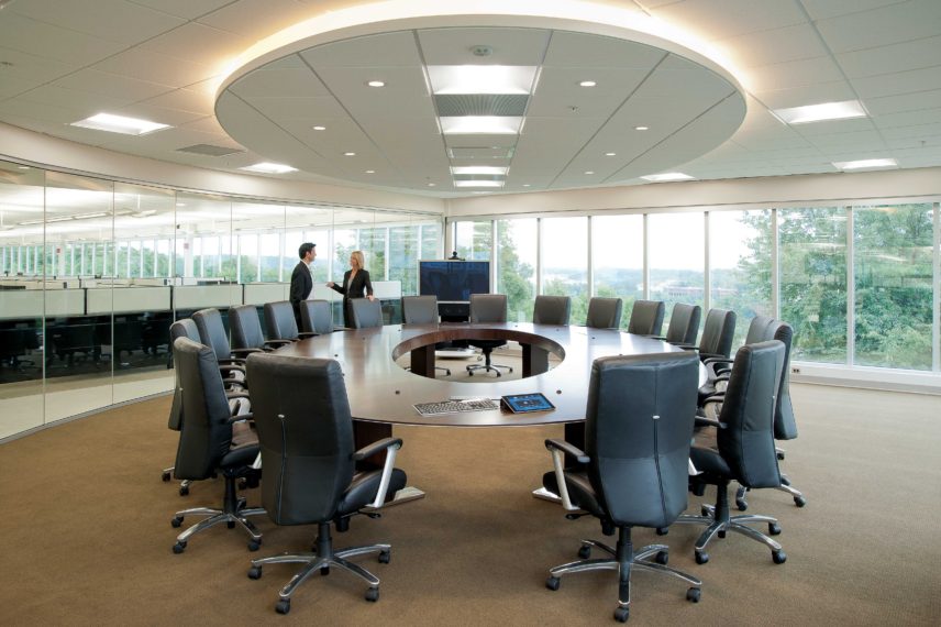 Large corporate meeting room with round table and chairs with two associates having conversation.