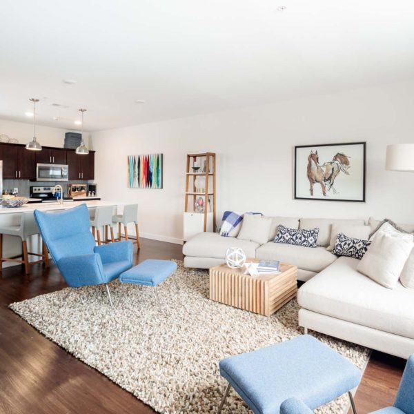 Apartment living room with chairs and couches overlooking a kitchen with high-end finishes.