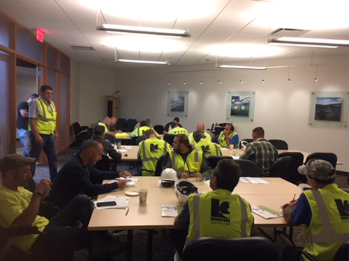 Large meeting room with construction workers sitting around tables for a training.