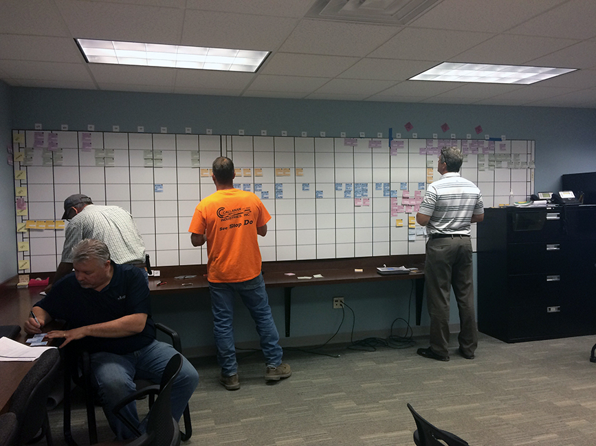 Four construction workers in a trailer in front of pull planning wall.