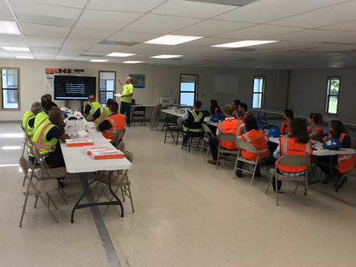 A large group of construction workers sitting at tables in a construction trailer.