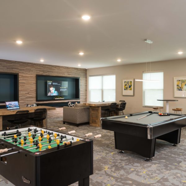 Gaming room with billiards and Foosball tables and large wall mounted tvs and lounge furniture.