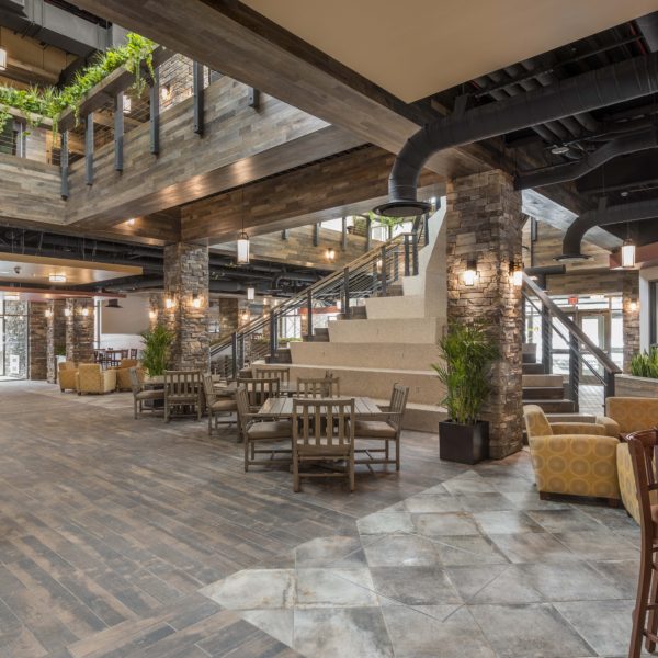 Lobby of dormitory with tables, chairs and exposed ceilings with a central stair case.