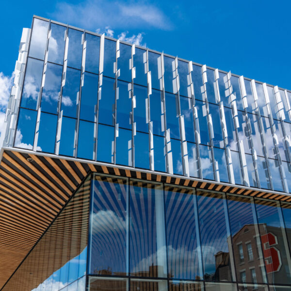 Photo of the exteriors of Syracuse University's  D’Aniello NVRC National Veterans Resource Center looking up towards the 3rd floor area and blue sky with white puffy clouds.